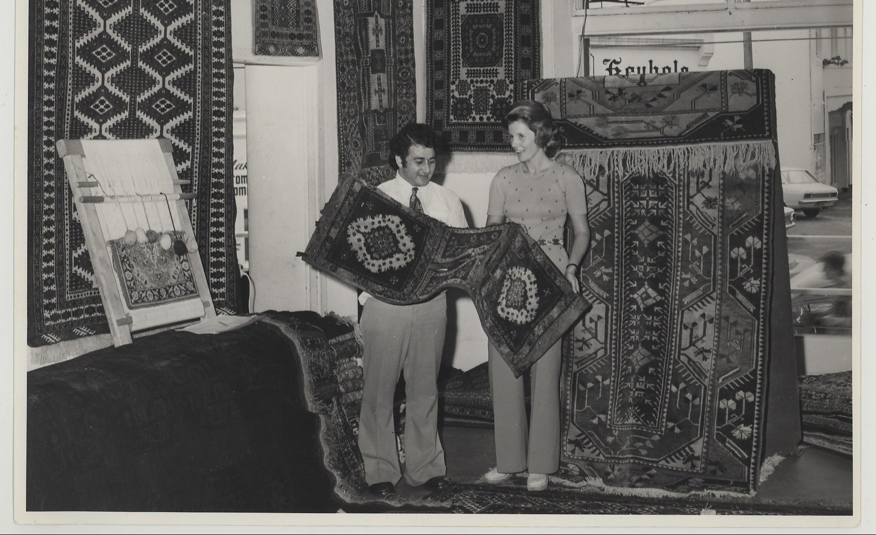 Two people examining rug in rug store with various antique rugs displayed on the walls